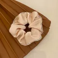 Close-up of an elegant champagne satin scrunchie with sparkling rhinestone trim - Off White