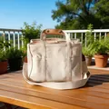 Primer plano detallado de un gran bolso de lona beige sobre una mesa de exterior. - Estilo Correa de Cuero / Beige