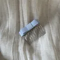 Close-up of an elegant light blue satin bow hair comb placed on a textured beige linen fabric - Blue
