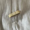 Close-up detail of a soft yellow satin bow hair comb on a textured linen background - Beige