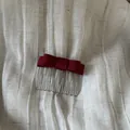 Detailed view of a dark red satin bow hair comb on white textured linen fabric. - Red