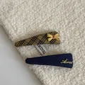 Detail view of stylish fabric hair clips with plaid bow and navy denim metal script. - Yellow-Black Striped Blue Triangle Hair Clips (Pair)