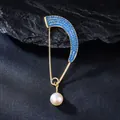 Close-up of gold curved brooch with blue rhinestones and pearl pendant on slate. - Blue