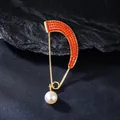 Detail of gold-tone curved brooch with orange rhinestones and white pearl pendant - Orange Red
