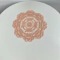 Detailed view of intricate lace embroidery on a rose gold round polyester table mat. - 28cm Round / Orange Red