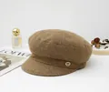 Detailed view of a stylish brown wool newsboy hat with a golden metal emblem accent - Camel Coffee
