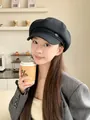 Eine modische Frau trägt eine stilvolle schwarze Newsboy-Mütze aus Kunstleder im Café - Schwarz