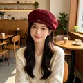 Close-up of a woman wearing a burgundy vintage suede beret in a cozy cafe. - Red