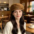 Detail shot of a brown suede beret with a metal tag worn by a woman in a warm cafe - Khaki