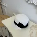 Detailed close-up view of a stylish white straw equestrian hat with black ribbon bow - White