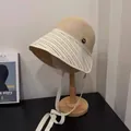 Beige straw bucket hat with black stripes and white ties displayed on a mannequin stand - Beige Stripe Patchwork