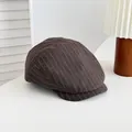 Vue détaillée d'une casquette gavroche marron à rayures rétro sur une table blanche épurée. - Café