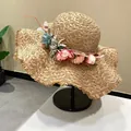 Hand-woven raffia sun hat with wide brim and colorful flower wreath on a black stand - Khaki