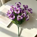 Detailansicht eines lila Stiefmütterchen-Kunststraußes mit Grün auf einem sonnigen Tisch - Hellviolett