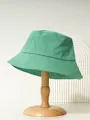 Detailed side view of a packable green cotton bucket hat on a wooden display stand. - M (56-58cm) / Green