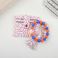 Detail view of baseball themed silicone bead bracelet and card holder set with tassel. - Orange Blue