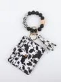 Detailed view of the cow print wallet keychain featuring beaded bracelet and tassel - Cow Pattern Style