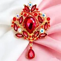 Dettaglio di una spilla a corona vintage con cristalli rossi su tessuto satin - Oro + Rosso
