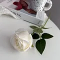 Close-up van een enkele witte kunstmatige zijden roos met groene bladeren op een tafel. - Wit