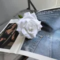 Elegante einzelne weiße künstliche Rose auf einer offenen Lifestyle-Zeitschrift - Reinweiß