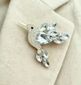 Elegant hummingbird brooch with sparkling crystals on beige fabric texture background. - White