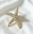 Detailopname van een gouden zeester speldje ingelegd met heldere strass steentjes - Goud + Witte Strass