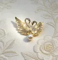 Elegant gold double swan brooch with sparkling crystals and a central pearl accent for coats - Gold