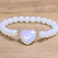 Detailopname van een armband van opaal-stijl kralen met een goudkleurige hartbedel. - Opaal
