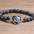 Close-up view of 8mm natural stone beaded bracelet with gold-framed heart charm - Snowflake Obsidian