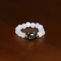 Detail shot of a handmade elastic ring featuring white shell pearls and a cat bead - Cat / White Black