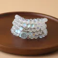 Gros plan d'un bracelet de 108 perles irisées avec pendentif lotus argenté sur bois - Pierre flash blanche