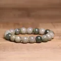 Macro detail of an 8mm natural Indian Agate beaded bracelet on a smooth wood surface - Green Straw Hat