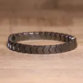 Close-up of a dark grey hematite chevron bead elastic bracelet placed on wood surface - Arrow Geometric Patchwork Style (#17)