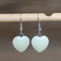 Gedetailleerd vooraanzicht van gladde hartvormige natuursteen oorbellen aan haakjes. - Hartstijl 2 (Witte Kristal)