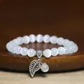 Detail shot of white cat eye stone beaded bracelet with vintage silver leaf charm. - Bright White