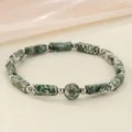 Close-up of a green marbled stone energy bracelet with silver beads on a silk background - Green Dot Stone