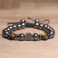 Macro-opname van een gevlochten hematiet armband met centraal Om-symbool en tijgeroog - Tijgeroog stenen armband