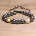 Detailopname van een hematiet kralenarmband met geslepen stenen en een Om-symbool. - Gele Aventurijn