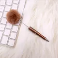 Cute brown fur pom-pom ball pen with metallic finish on white faux fur desk background - Pearl Camel