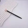 Sleek black ballpoint pen with a rose gold heart topper, displayed on a wavy white tray. - Rose Gold Accessories / Black
