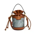 A close-up view of a cylindrical bucket bag featuring denim and brown leather patchwork. - Denim Blue