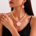 Filigranes Schmuckset mit rosa Frangipani-Blütenkette und Ohrringen an einem Model - Rosa