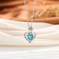 Vista detallada del collar de corazón plateado con cristal azul y rosa sobre seda blanca - Estilo Corazón / Azul lago