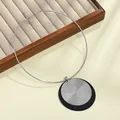 Detailansicht eines silbernen Halsreifs mit strukturiertem Doppelscheibenanhänger. - Halskette / Silber