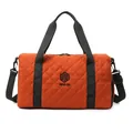 Close-up of orange quilted travel bag with black handles and adjustable shoulder strap - Orange