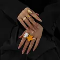 Elegante Detailansicht goldener Flüssig-Lava-Ringe mit oranger Blume und Perle - Stil 4 (BGZ-267) / Gold