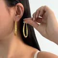 Close-up shot of elegant gold-tone textured teardrop hoop earrings worn by a model. - Style 1 (KZEH-6582) / Gold