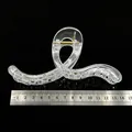 Macro view of a transparent PC hair claw clip base with a metal ruler for scale - Curved Ribbon Shape / 13cm