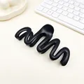 Detailed view of a matte black wave-shaped hair claw clip on a minimalist desk setup - Matte Black