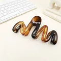 Detailed macro view of a tortoiseshell wavy hair claw clip with a glossy amber finish. - Glossy Amber
